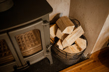 Load image into Gallery viewer, Firewood in a basket next to a woodburning stove.